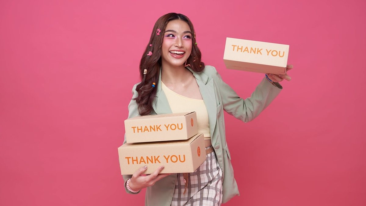 Phụ nữ trẻ cười tươi, ôm các hộp giấy in chữ THANK YOU, phong cách ảnh quảng cáo bán hàng online
